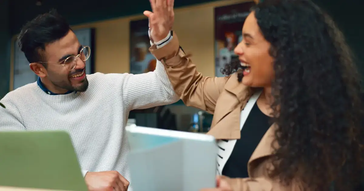 a couple high fiving celebrating their online success in front of a laptop